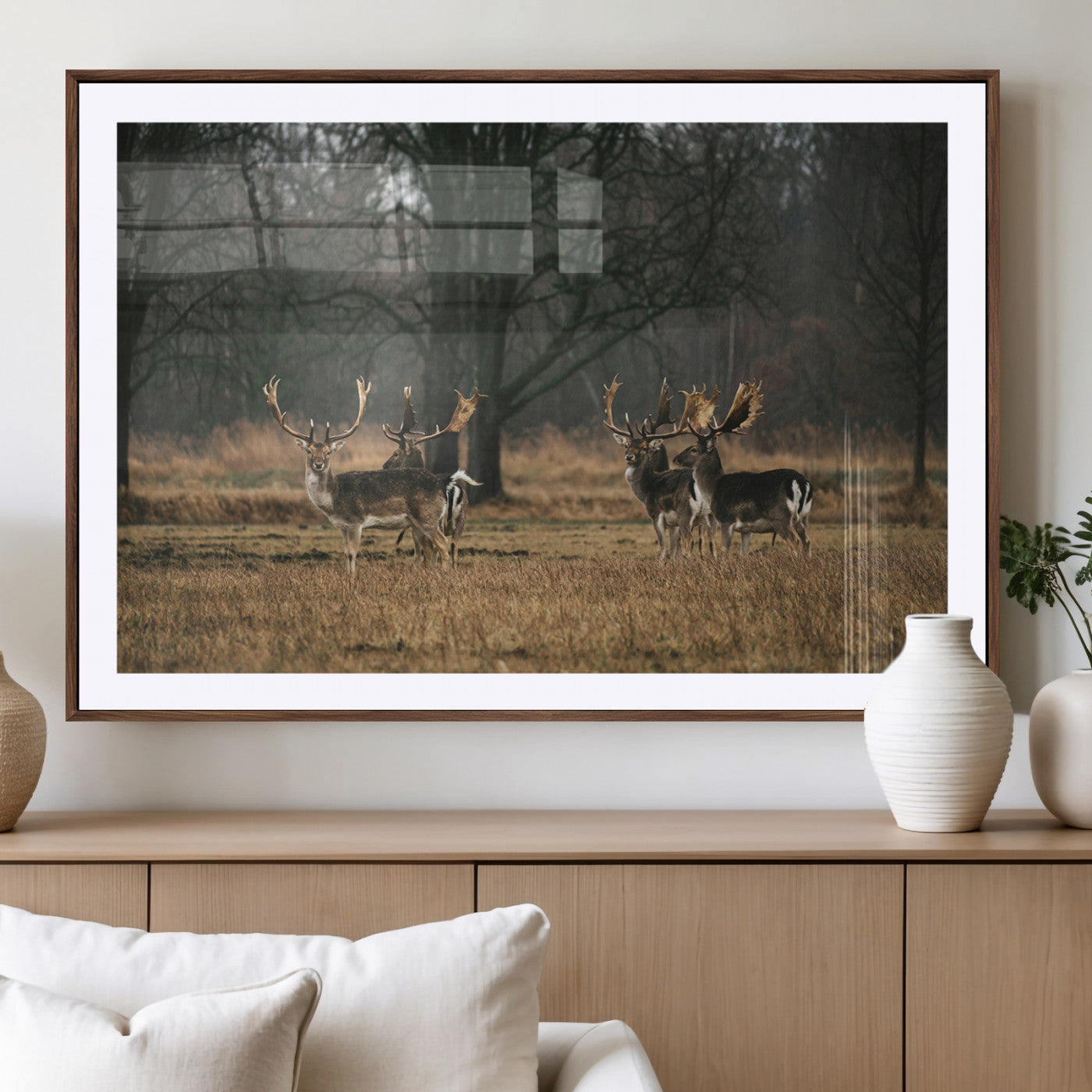 A group of majestic deer standing in a golden field with bare trees in the background, creating a peaceful woodland scene.