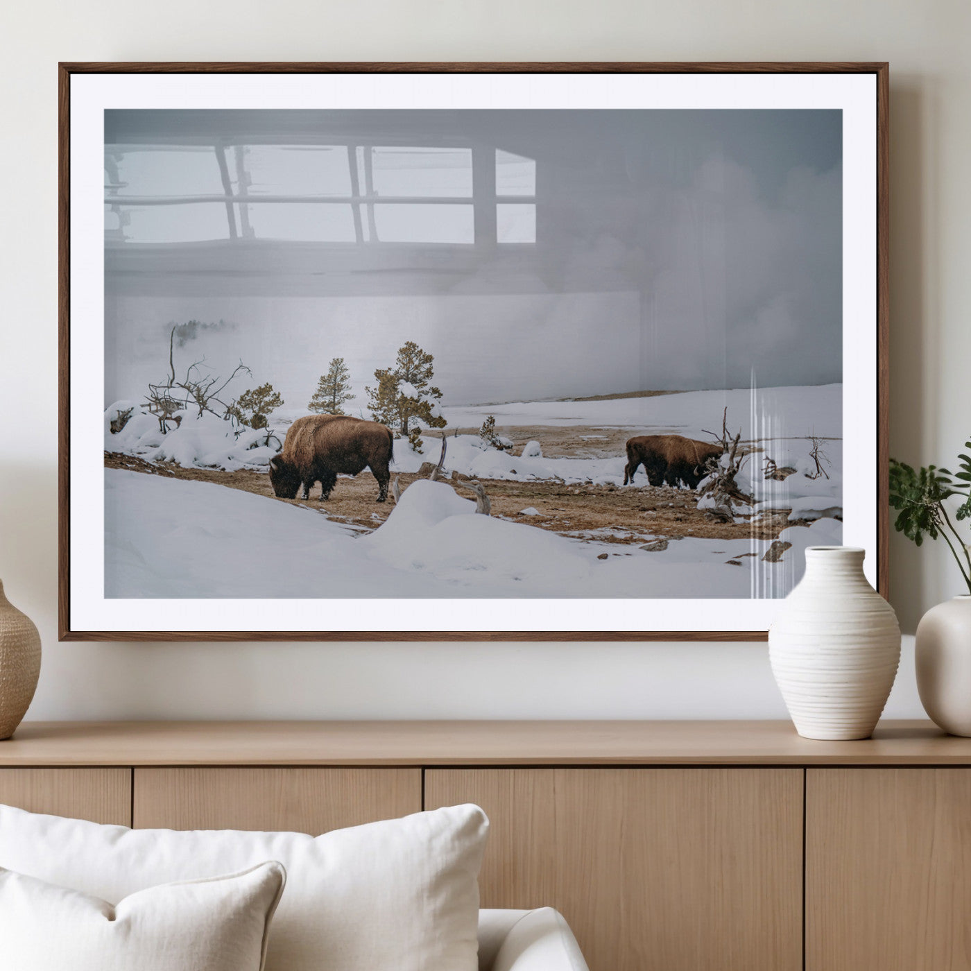 Two bison grazing in a snowy open landscape with misty hills in the background, creating a peaceful and rustic winter scene.