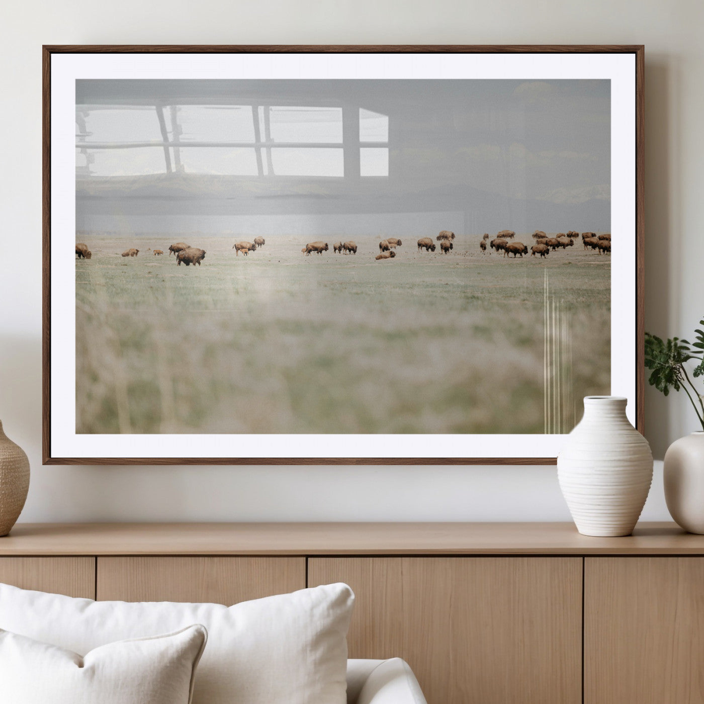 A herd of bison grazing in an open prairie with distant mountains under a soft sky, creating a serene and rustic Western landscape.