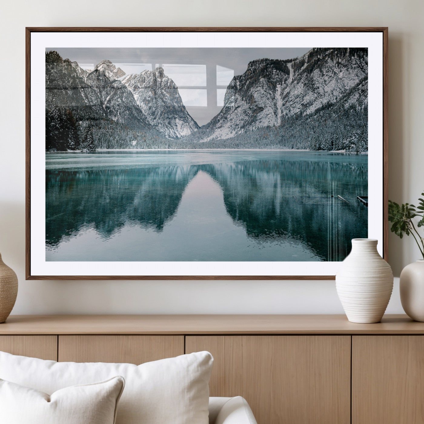 Crystal-clear alpine lake reflecting snow-covered mountains, surrounded by evergreen trees, creating a serene and tranquil winter landscape.