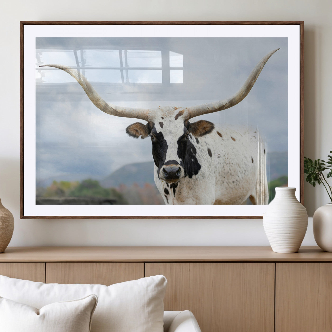 Close-up of a Texas Longhorn with curved horns, black and white markings, set against a cloudy sky and distant hills, perfect for rustic decor.