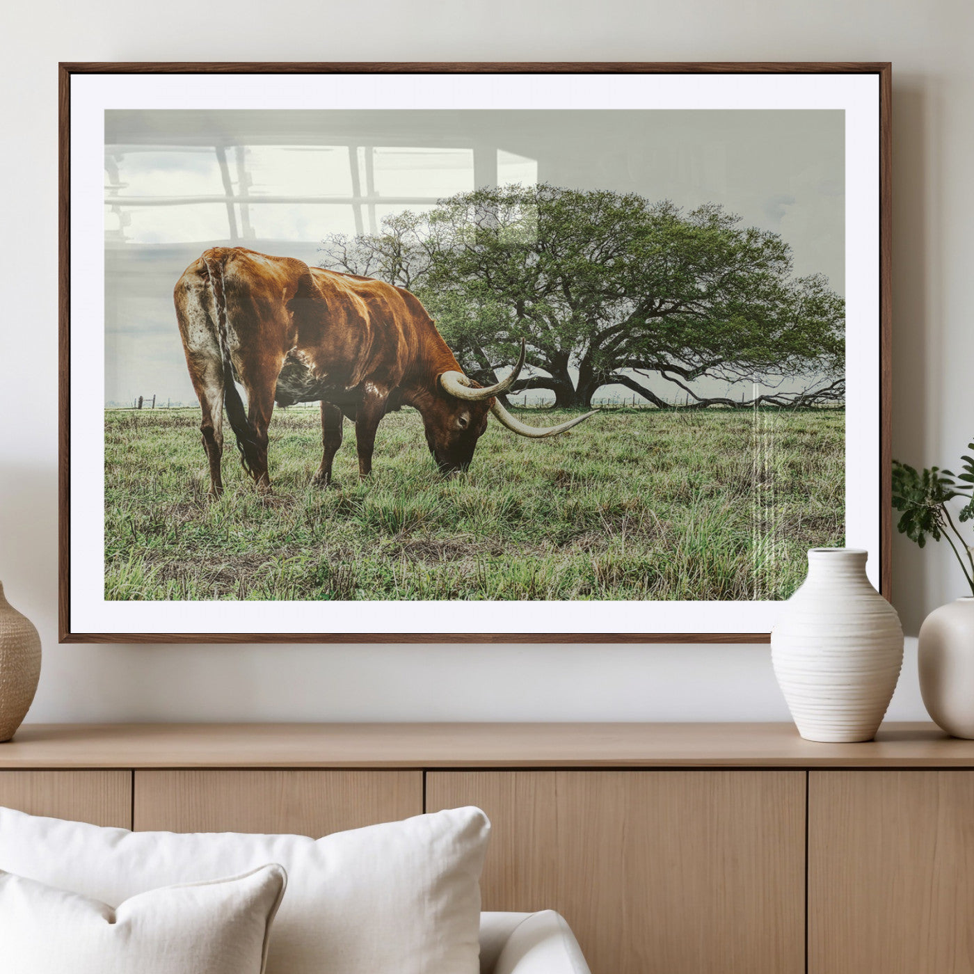 A Texas Longhorn grazing in a green pasture with a large tree in the background, evoking a rustic Western and farmhouse aesthetic.