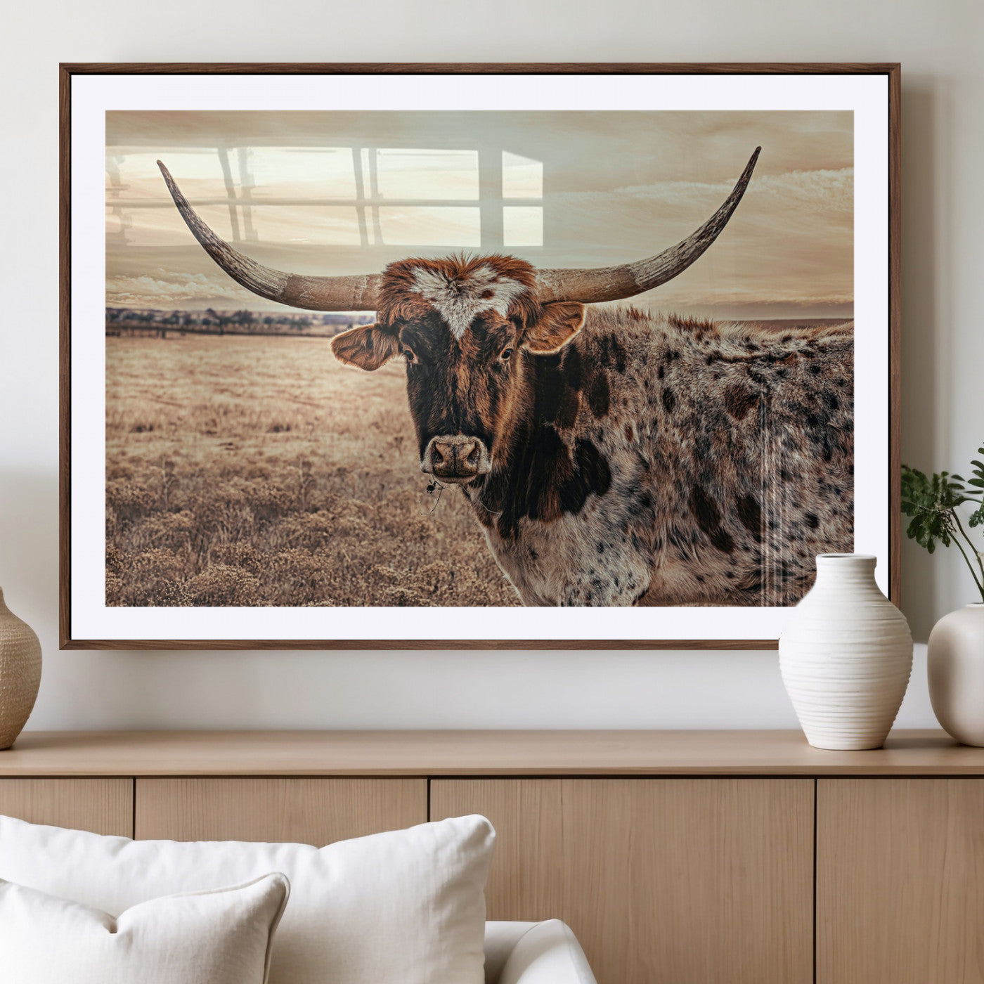 Close-up of a longhorn cow with distinctive curved horns standing in a dry grass field under a cloudy sky.