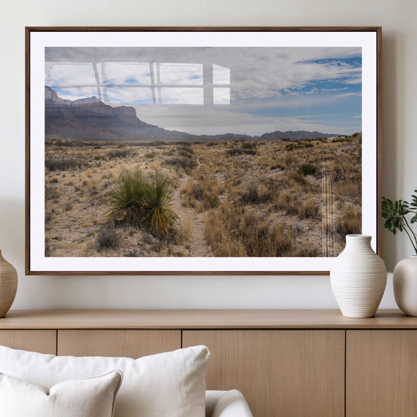 A scenic desert landscape with dry grasses, scattered shrubs, and a distant mountain range under a partly cloudy blue sky.