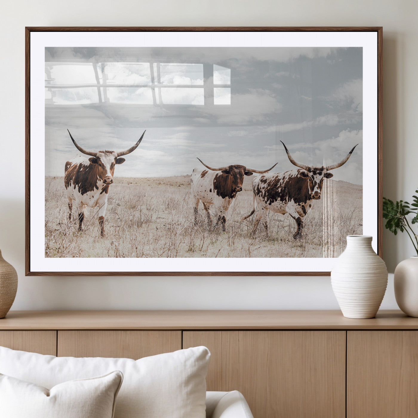 Three Texas Longhorn cattle walking through a dry grassy field under a partly cloudy sky.