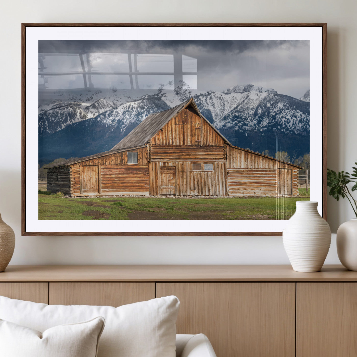 A stunning wall art canvas print featuring a rustic wooden barn set against a backdrop of snow-capped mountains under a dramatic cloudy sky, perfect for adding a touch of rural charm to any space.