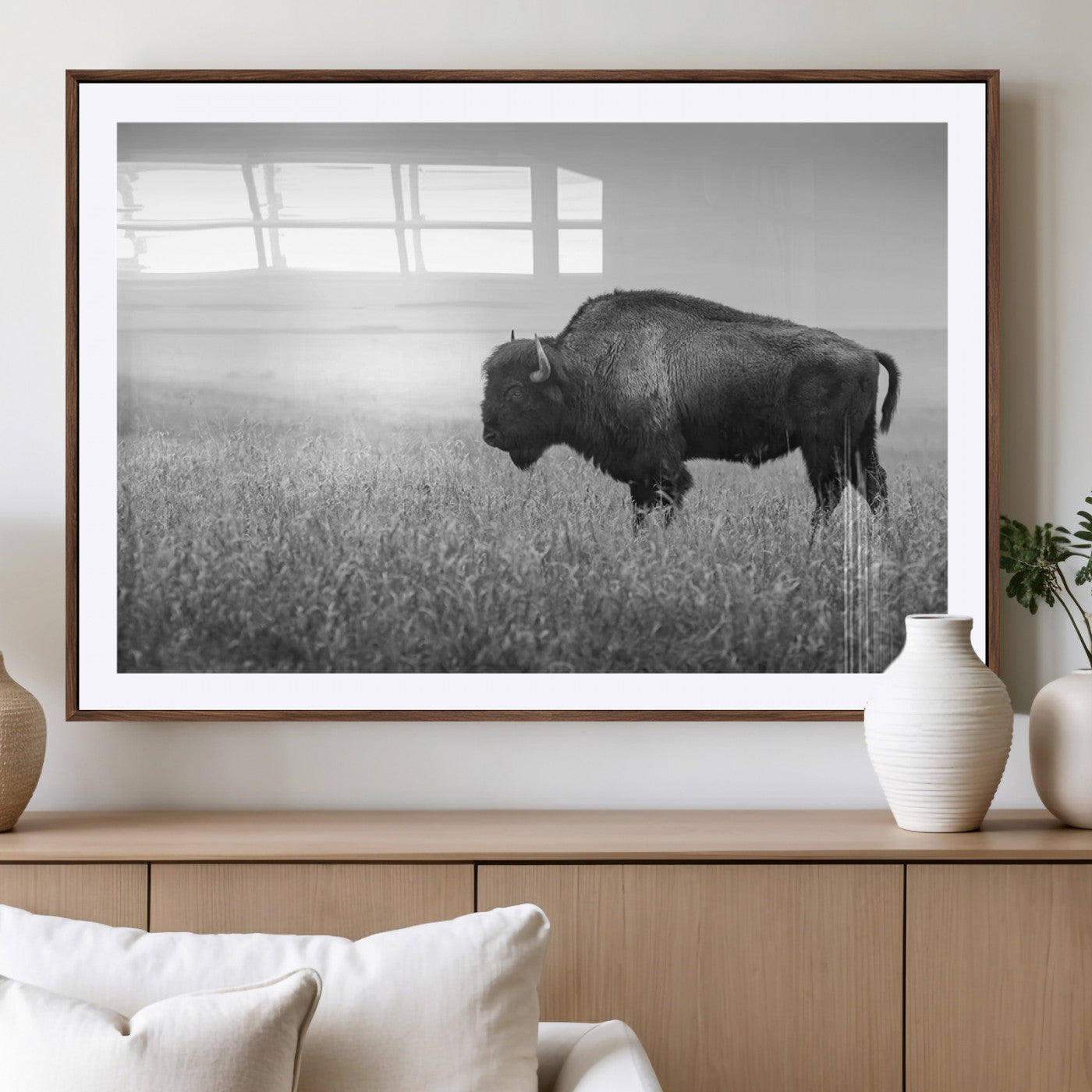 "Black and white image of a bison grazing in a vast field under an overcast sky."