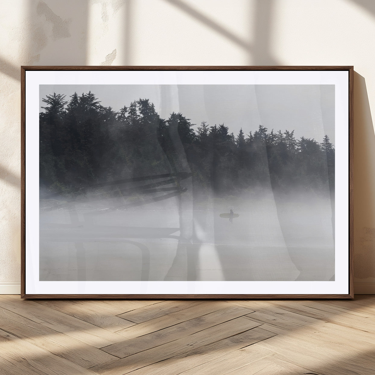 A lone surfer carrying a board through a misty shoreline, surrounded by dense trees and fog, creating a peaceful and mysterious coastal scene.