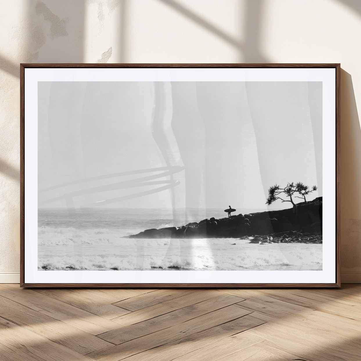 Black and white photo of a surfer standing on rocky cliffs, gazing at the waves, embodying the spirit of adventure and solitude.