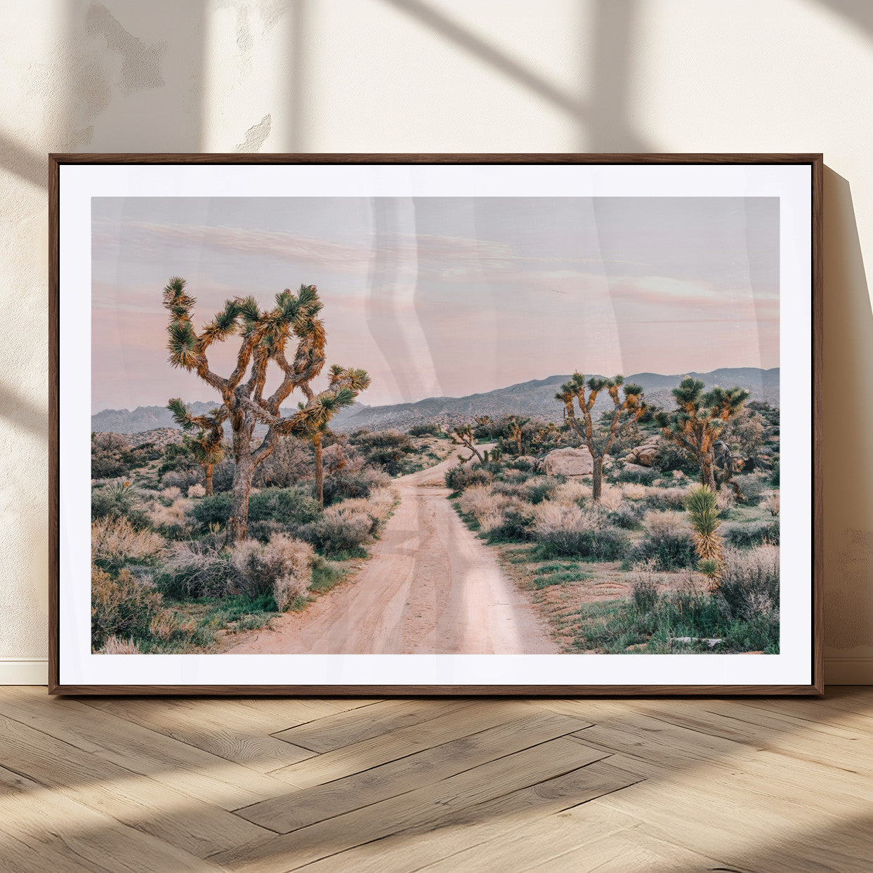 A dusty road winding through Joshua Tree National Park, framed by iconic twisted trees and warm desert tones under a soft pastel sky.