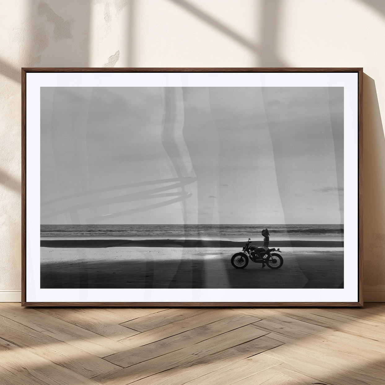 A motorcyclist on a vast beach, gazing at the ocean, capturing a moody and tranquil coastal adventure in black and white.