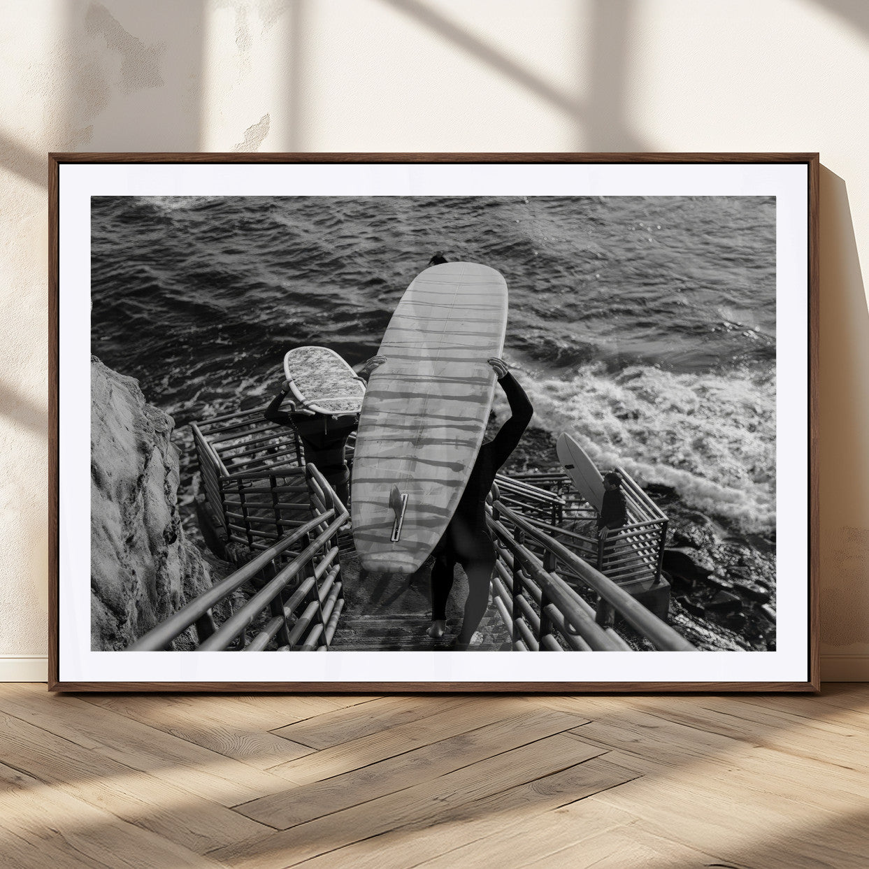 Black and white photo of surfers carrying boards down a rugged cliffside stairway, capturing a bold and adventurous coastal scene.