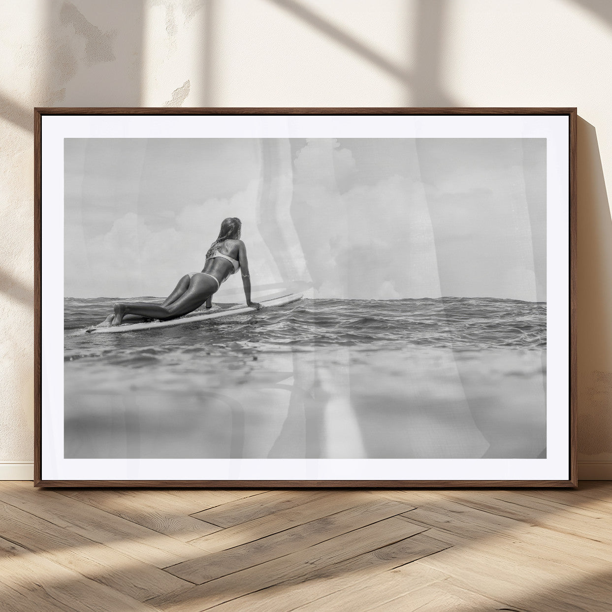 A black and white ocean scene featuring a surfer girl waiting on her board, gazing at the horizon, capturing a tranquil and adventurous coastal moment.