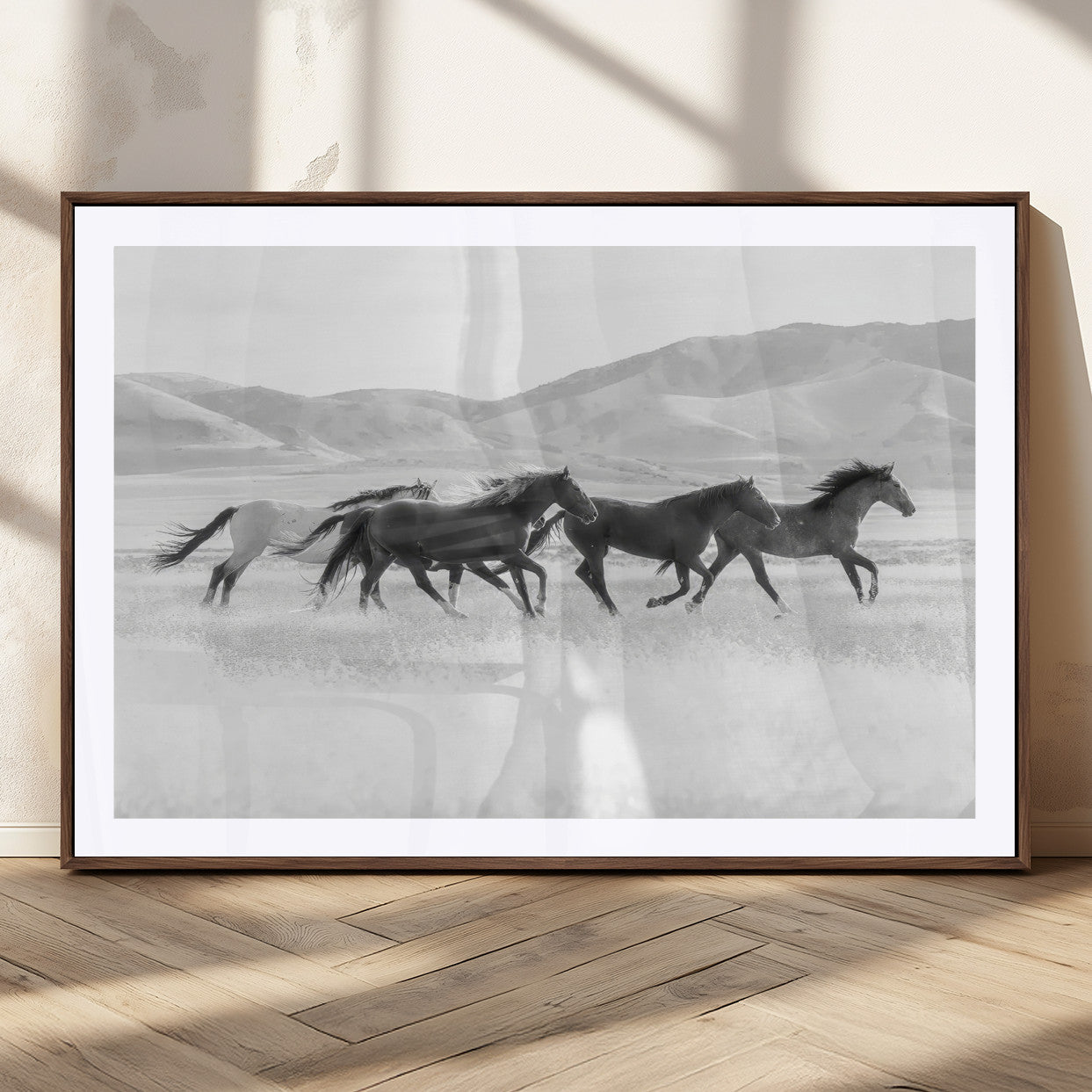 A black and white image of wild horses running freely across an open grassland, capturing the power and beauty of untamed nature in a rustic western setting.