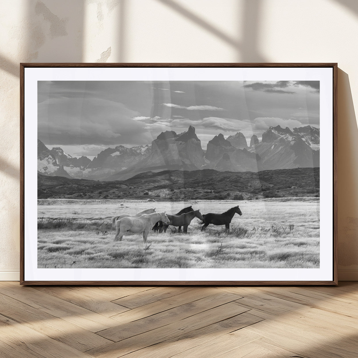 A black and white landscape of wild horses grazing in a vast grassland with towering mountains in the background, creating a moody and rustic western aesthetic.