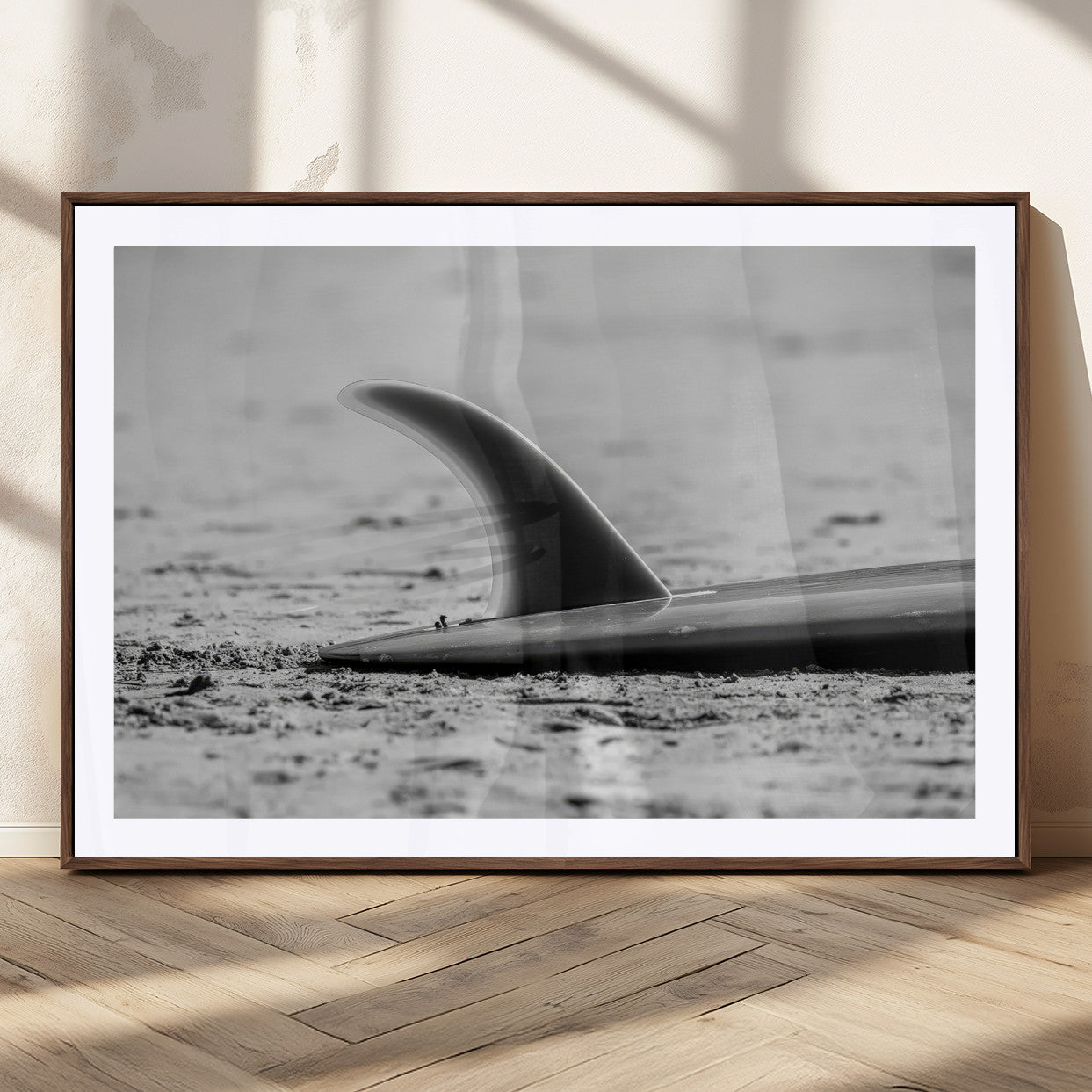 A black and white close-up of a surfboard fin resting on the sandy shore, highlighting minimalist beach aesthetics and classic surf culture.