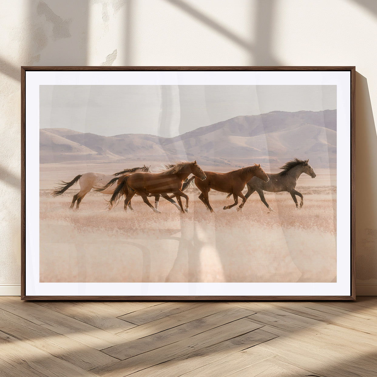 A herd of wild horses galloping through a sunlit desert plain with mountains in the background, perfect for rustic or western-themed wall decor.