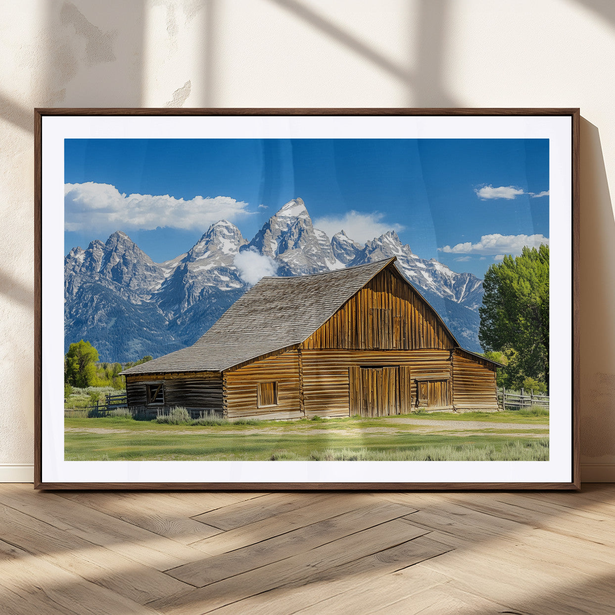 A rustic wooden barn sits in front of towering mountain peaks under a clear blue sky, perfect for farmhouse or cabin style interiors.