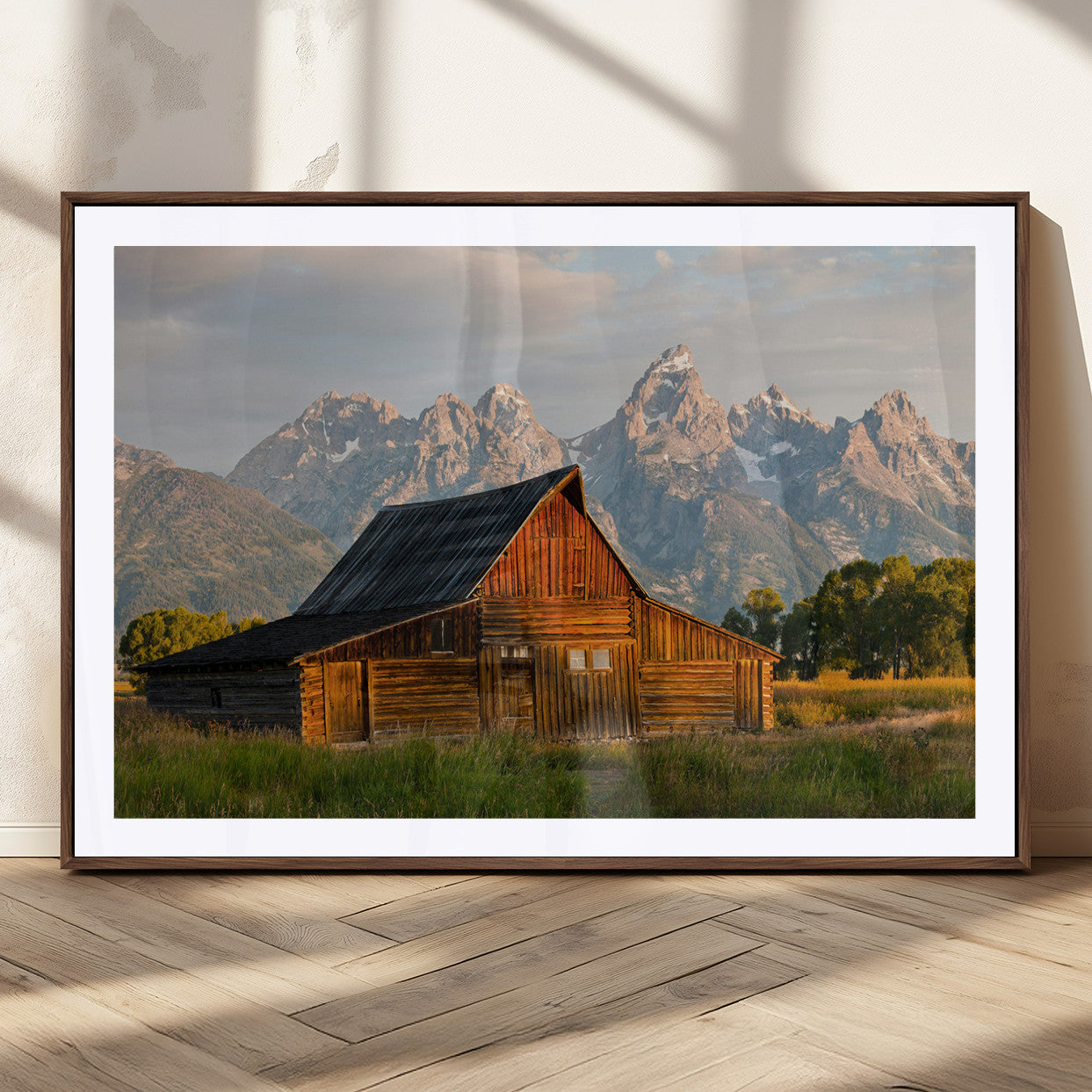 Rustic wooden barn set against towering mountain peaks under warm golden light, creating a peaceful Western countryside scene.