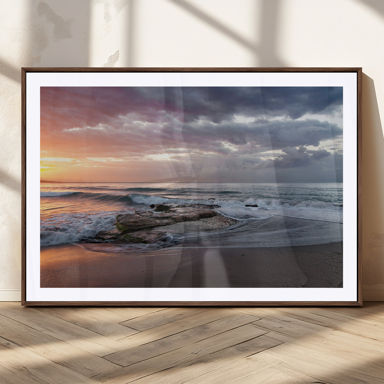 Dramatic sunset over a rocky shoreline with ocean waves gently reaching the sandy beach, creating a serene and coastal atmosphere.