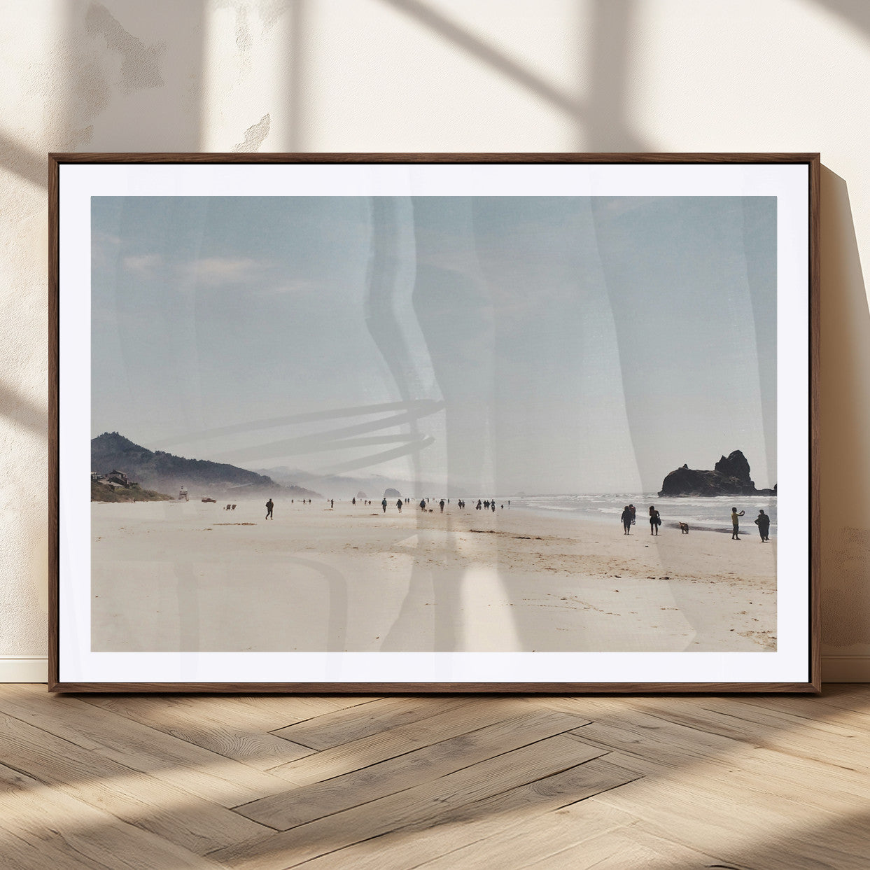 A serene beach with soft sand, misty mountains, and scattered people walking along the shoreline, creating a peaceful coastal landscape.