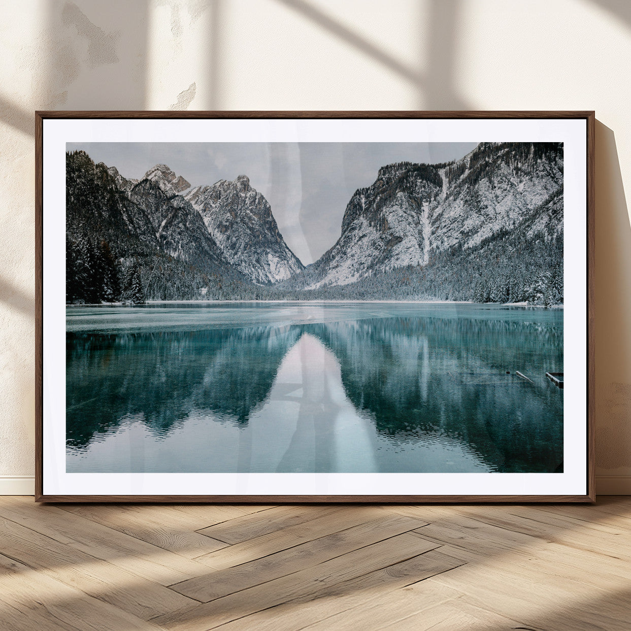 Crystal-clear alpine lake reflecting snow-covered mountains, surrounded by evergreen trees, creating a serene and tranquil winter landscape.
