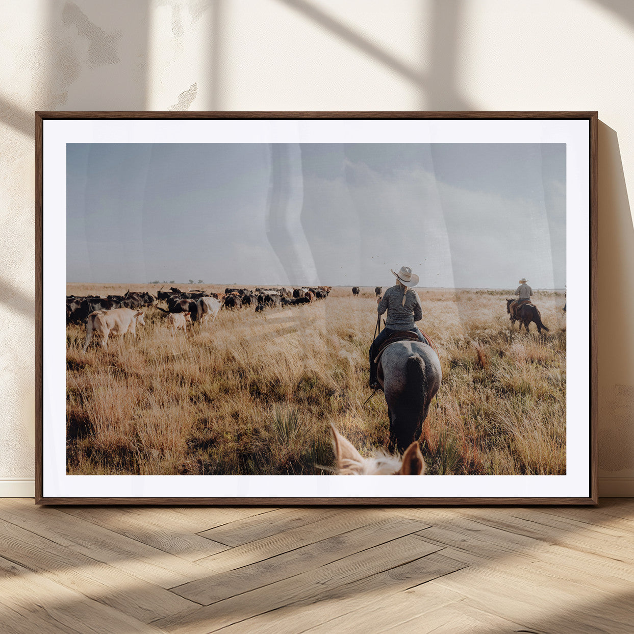 A cowboy and cowgirl on horseback herding cattle through golden grasslands, capturing a rustic and authentic Western ranch lifestyle.