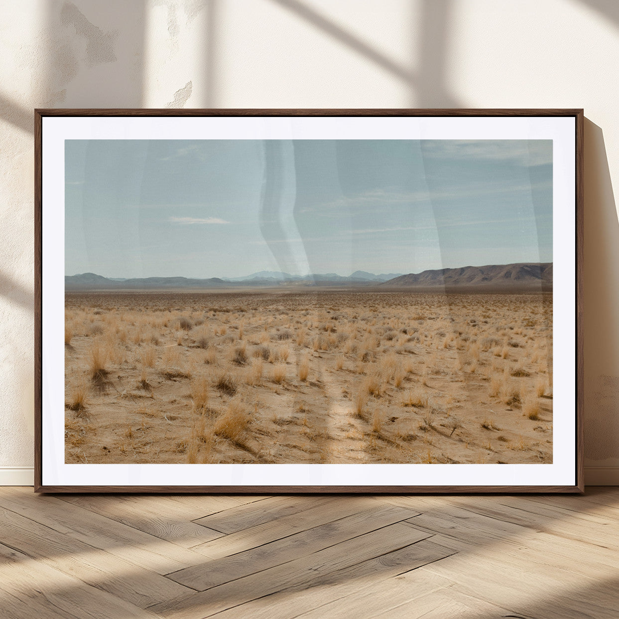 Expansive desert landscape with scattered dry grass and distant mountain range under a pale blue sky – Wall Art Canvas Print.