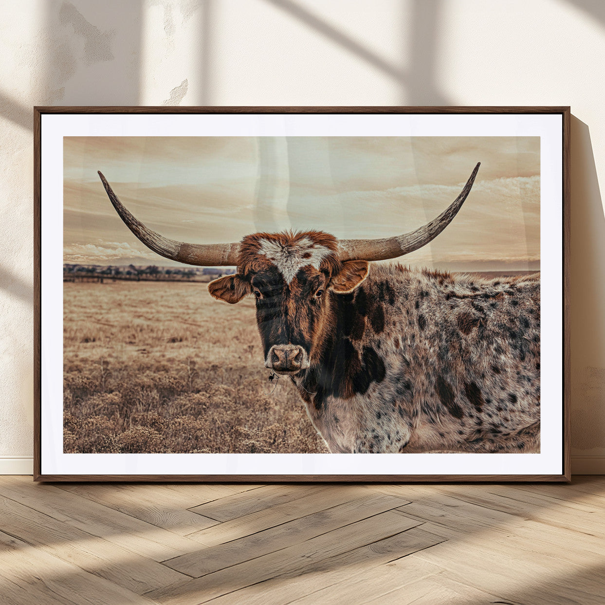 Close-up of a longhorn cow with distinctive curved horns standing in a dry grass field under a cloudy sky.