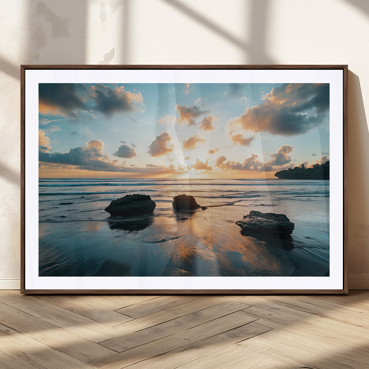 A serene beach at sunset with vibrant clouds, calm water, and rocks in the foreground reflecting the warm colors of the setting sun.