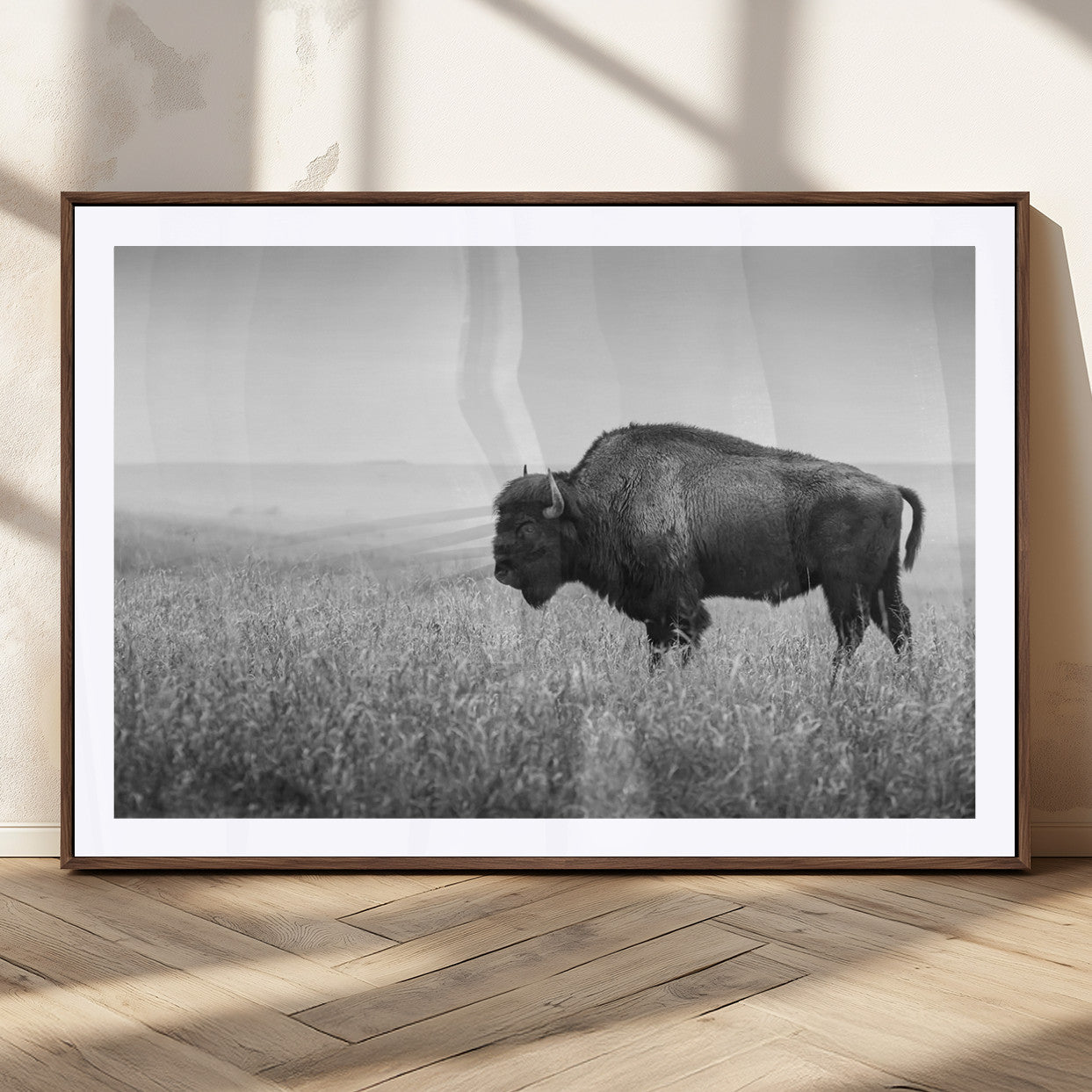 "Black and white image of a bison grazing in a vast field under an overcast sky."