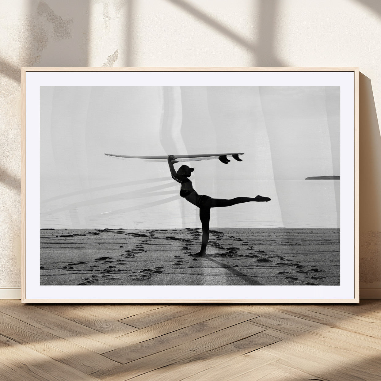 A woman balances a surfboard on her head while striking a yoga pose on the beach, silhouetted against a calm ocean horizon.