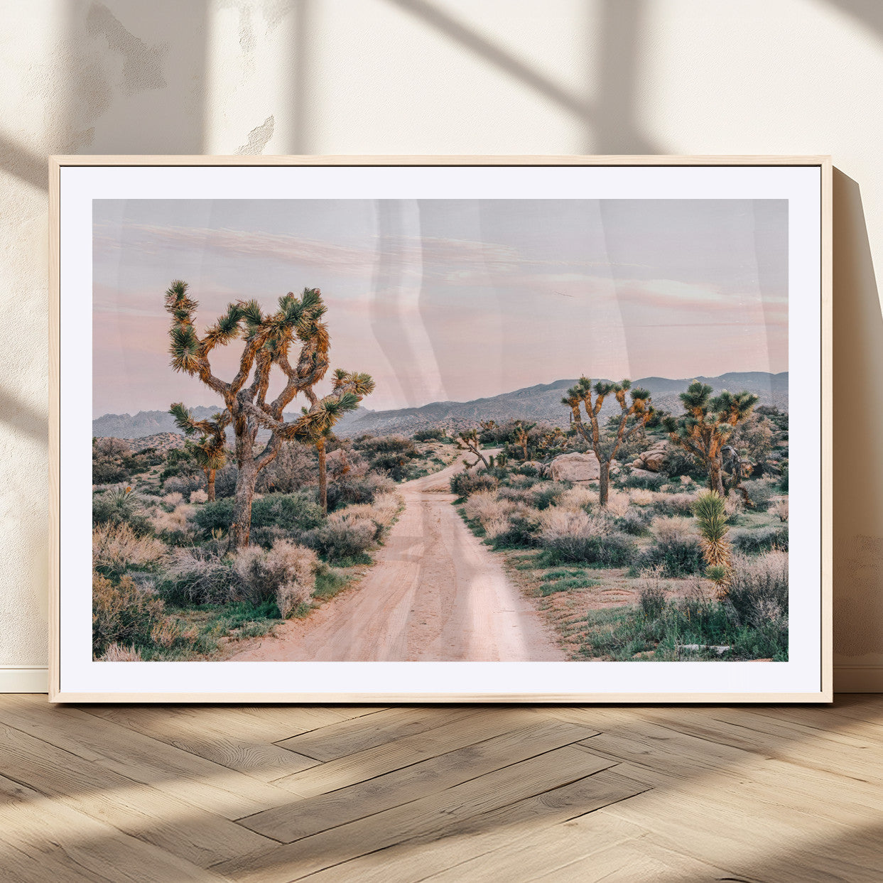 A dusty road winding through Joshua Tree National Park, framed by iconic twisted trees and warm desert tones under a soft pastel sky.
