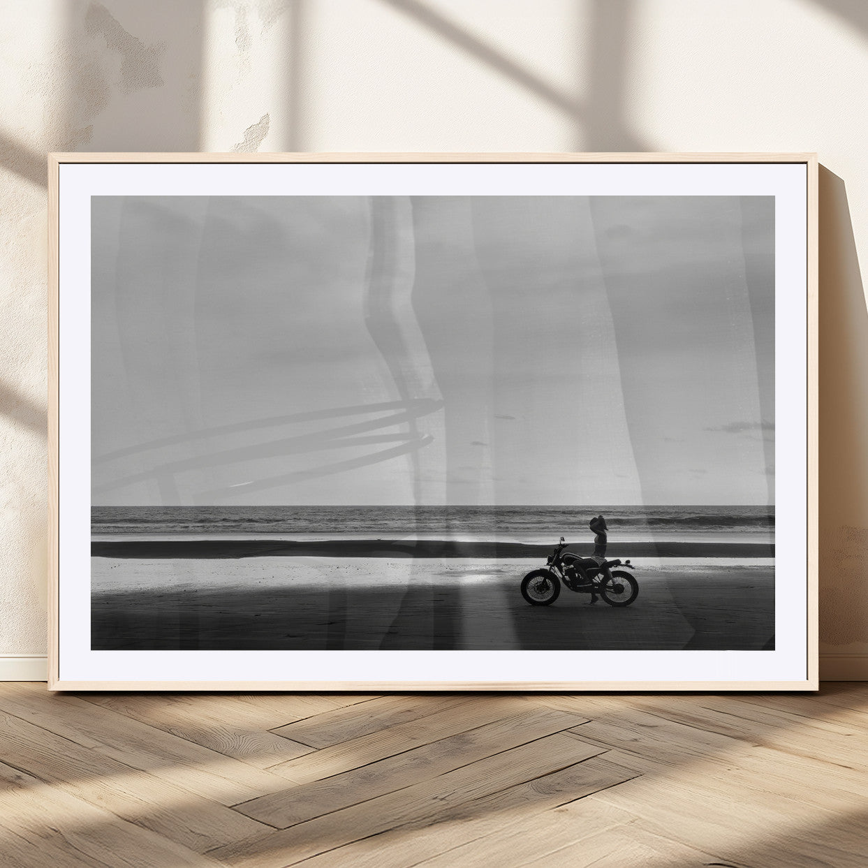 A motorcyclist on a vast beach, gazing at the ocean, capturing a moody and tranquil coastal adventure in black and white.