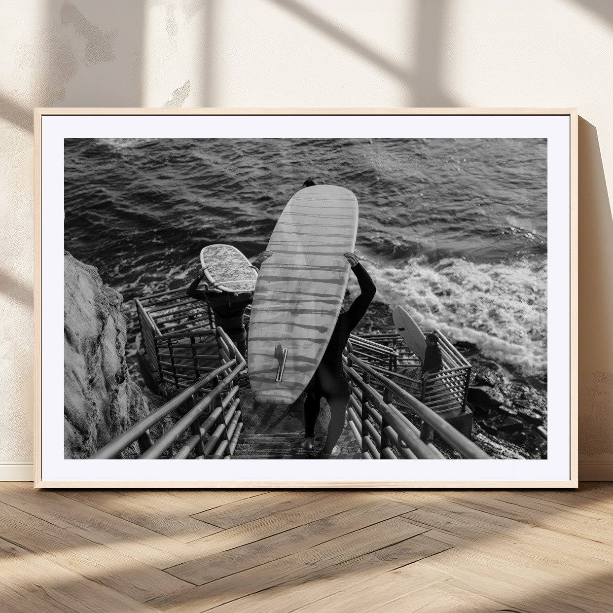Black and white photo of surfers carrying boards down a rugged cliffside stairway, capturing a bold and adventurous coastal scene.
