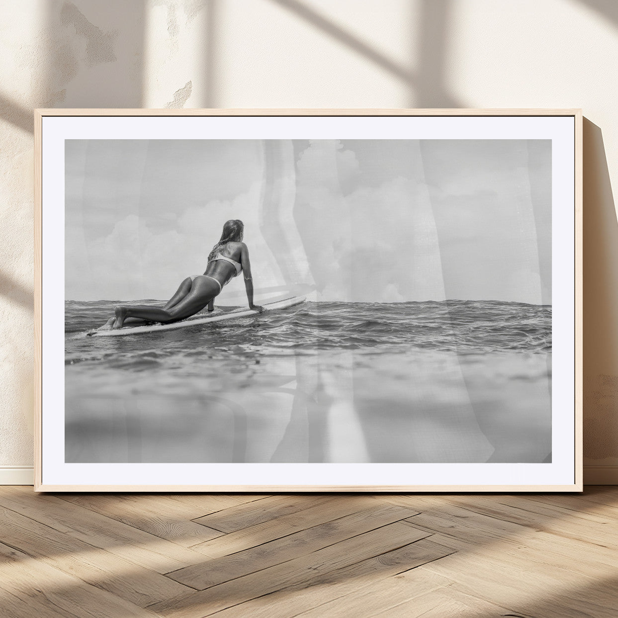 A black and white ocean scene featuring a surfer girl waiting on her board, gazing at the horizon, capturing a tranquil and adventurous coastal moment.