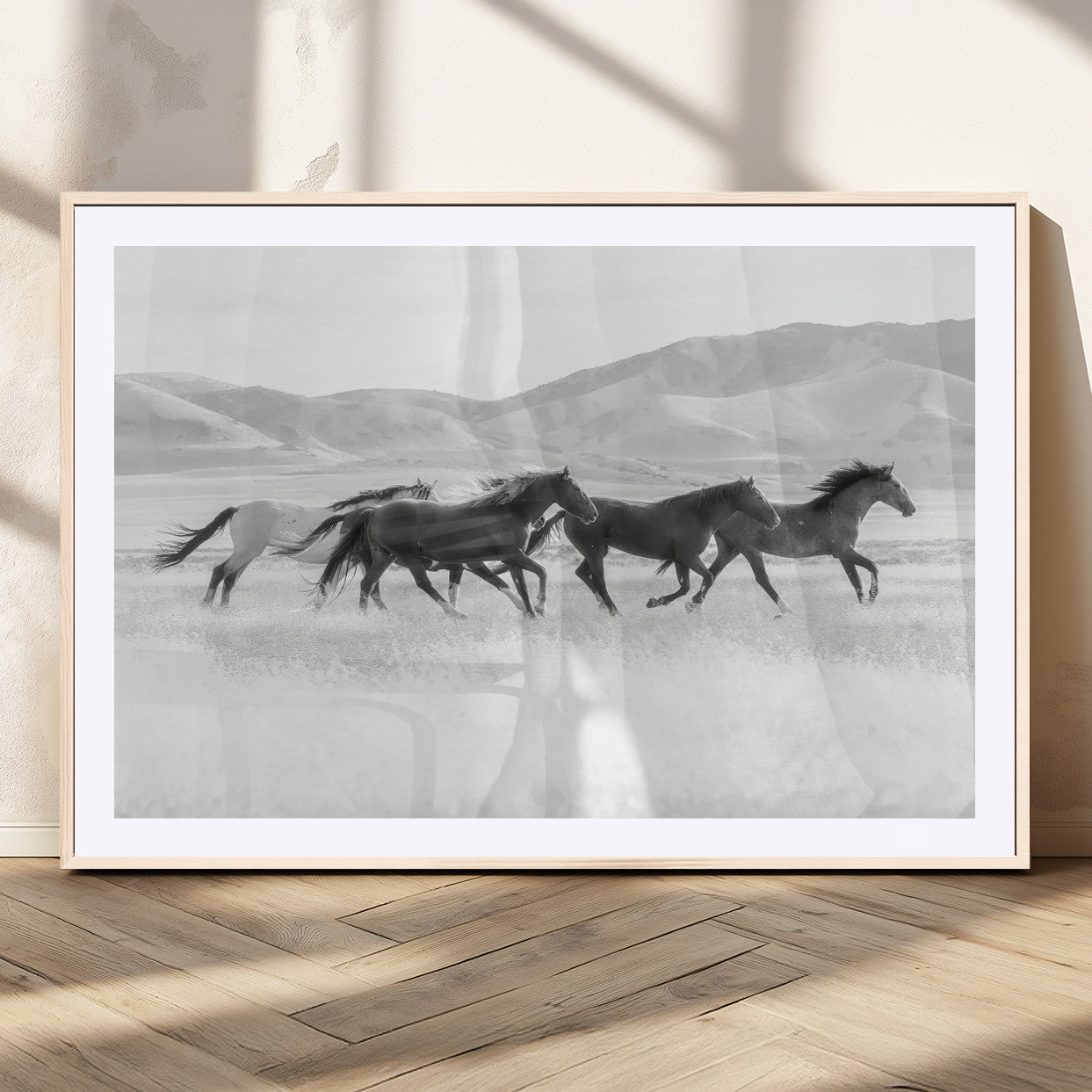 A black and white image of wild horses running freely across an open grassland, capturing the power and beauty of untamed nature in a rustic western setting.