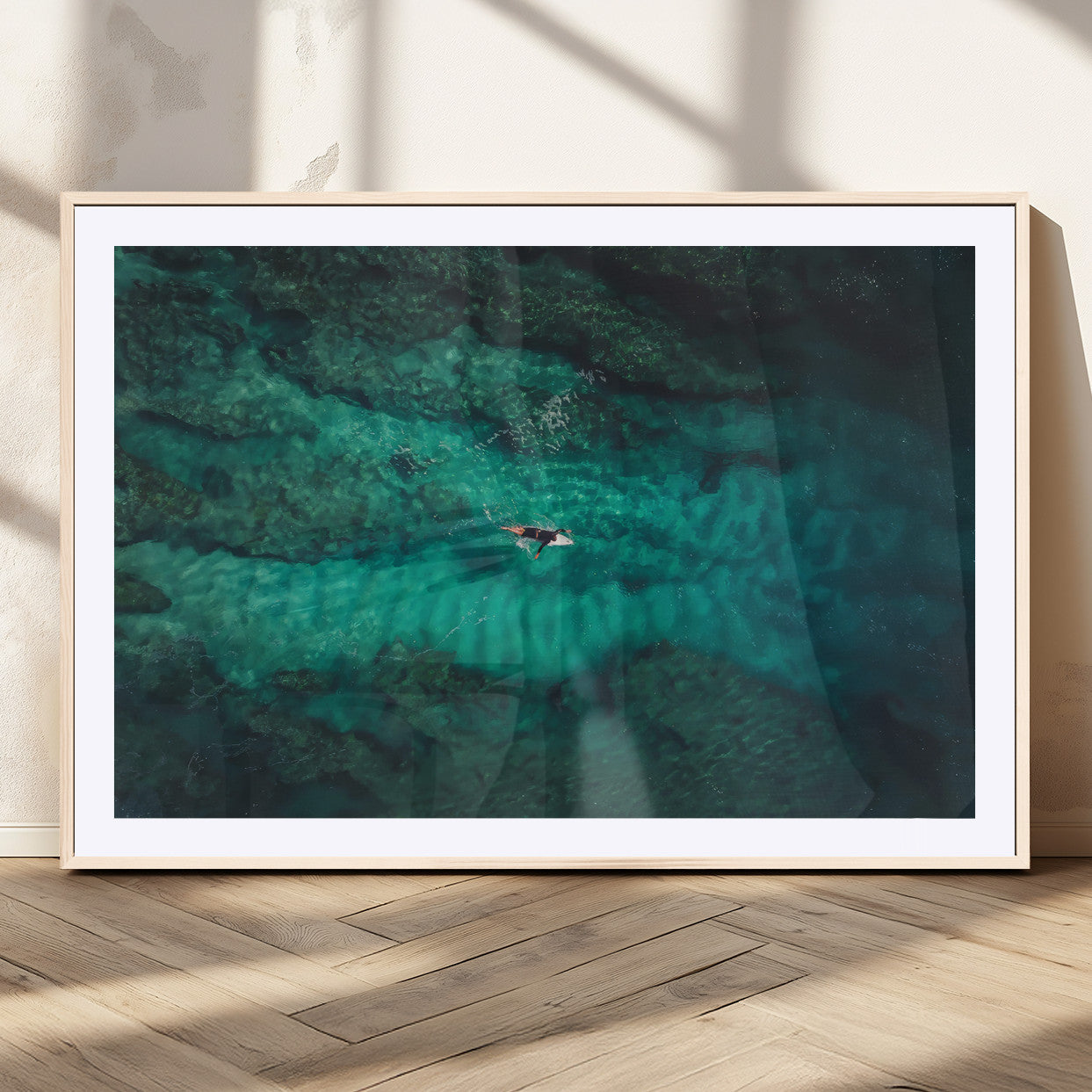 An aerial view of a solo surfer paddling through crystal-clear turquoise waters over a sunlit reef, capturing the beauty and serenity of open water surfing.