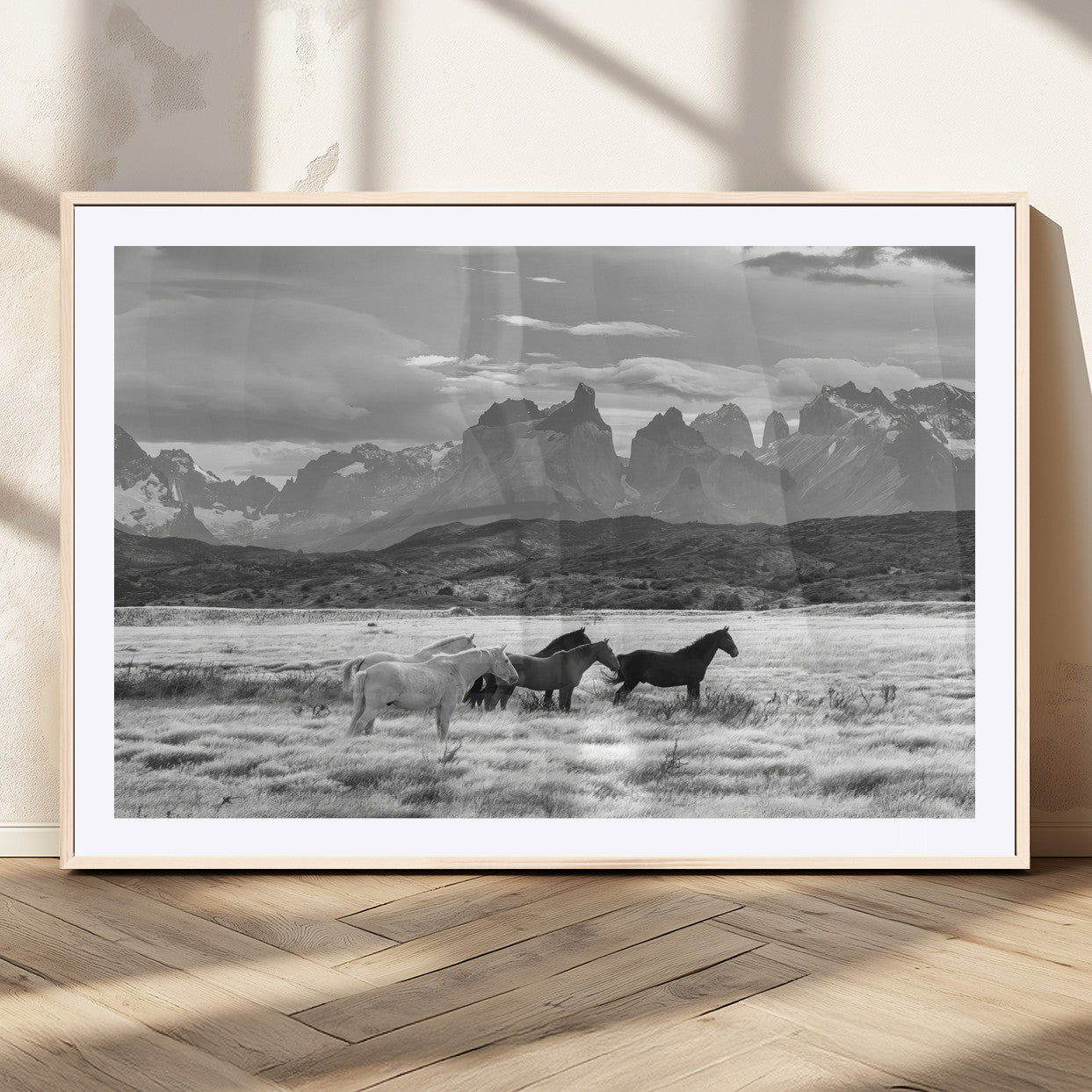 A black and white landscape of wild horses grazing in a vast grassland with towering mountains in the background, creating a moody and rustic western aesthetic.