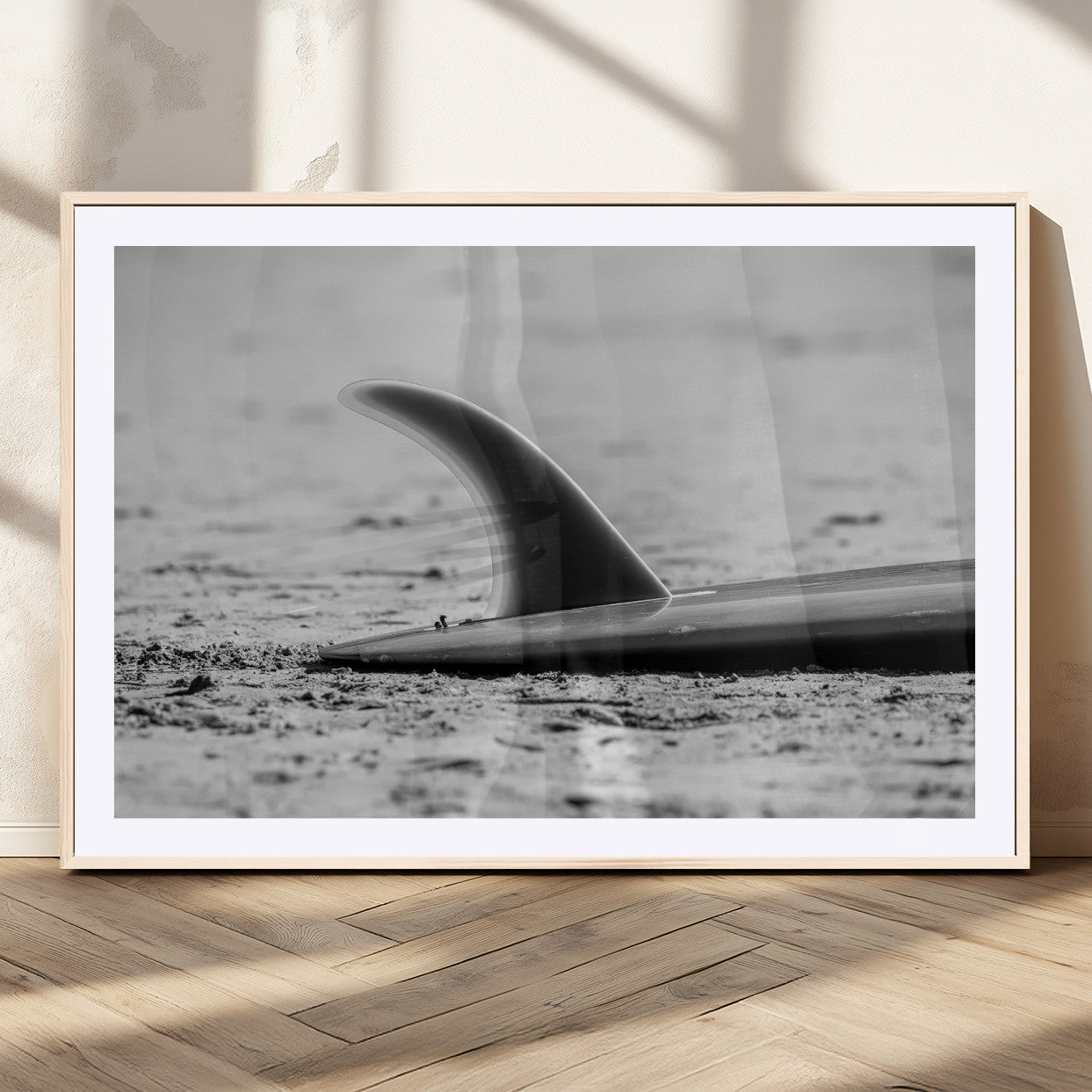 A black and white close-up of a surfboard fin resting on the sandy shore, highlighting minimalist beach aesthetics and classic surf culture.