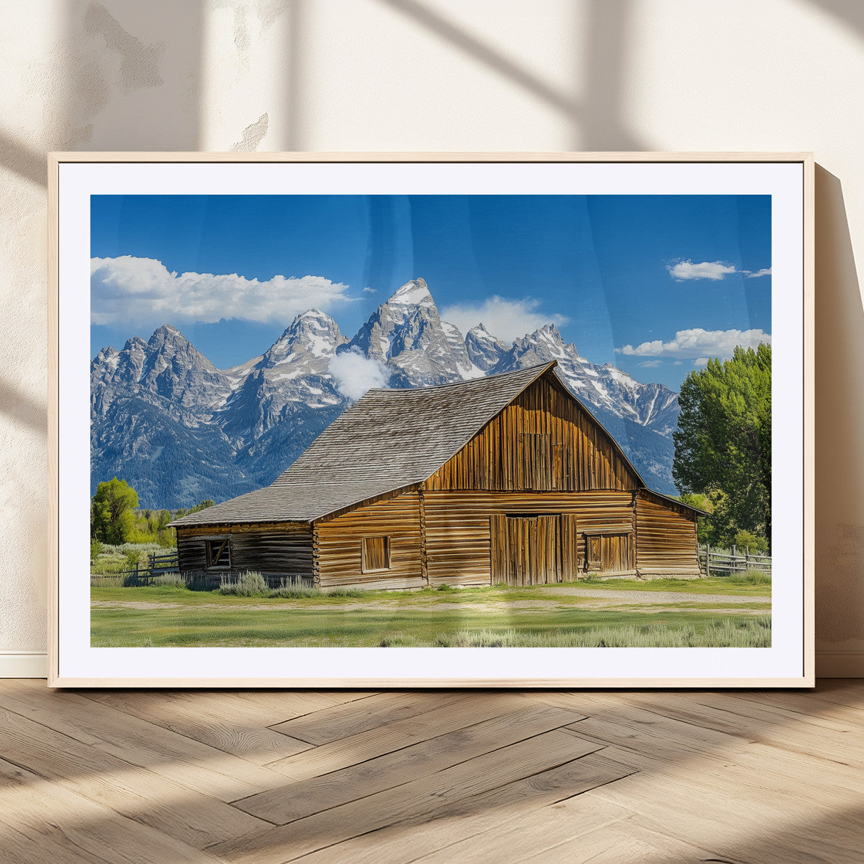 A rustic wooden barn sits in front of towering mountain peaks under a clear blue sky, perfect for farmhouse or cabin style interiors.