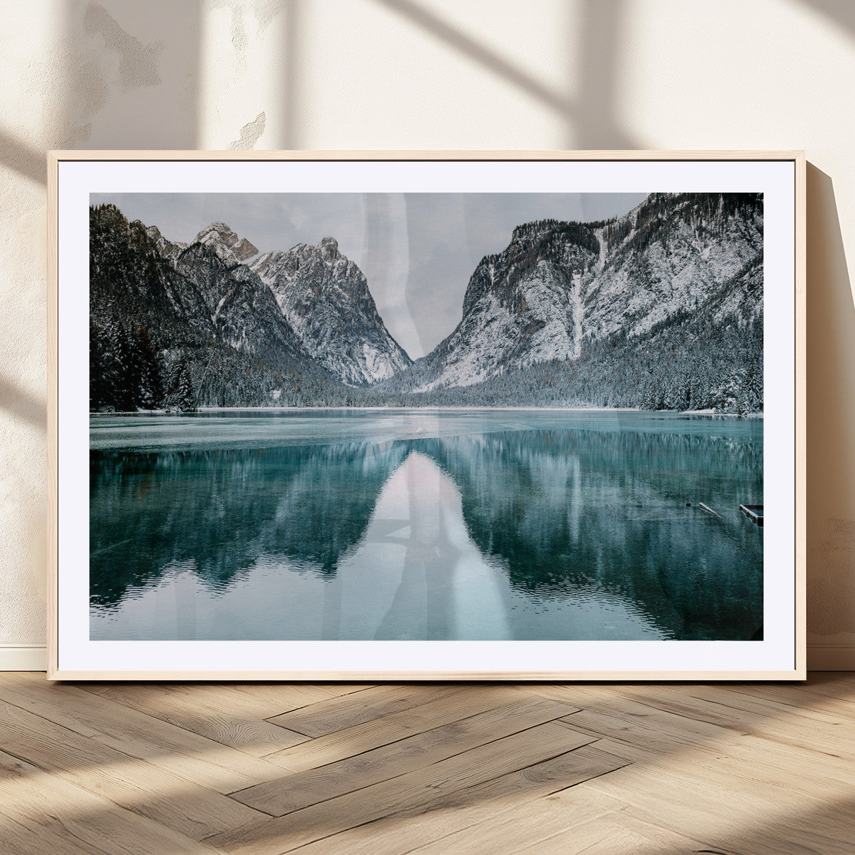 Crystal-clear alpine lake reflecting snow-covered mountains, surrounded by evergreen trees, creating a serene and tranquil winter landscape.