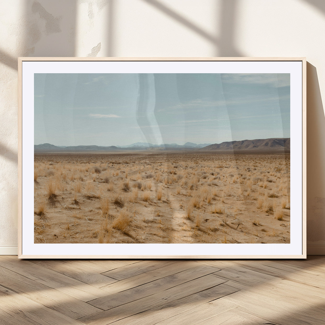 Expansive desert landscape with scattered dry grass and distant mountain range under a pale blue sky – Wall Art Canvas Print.