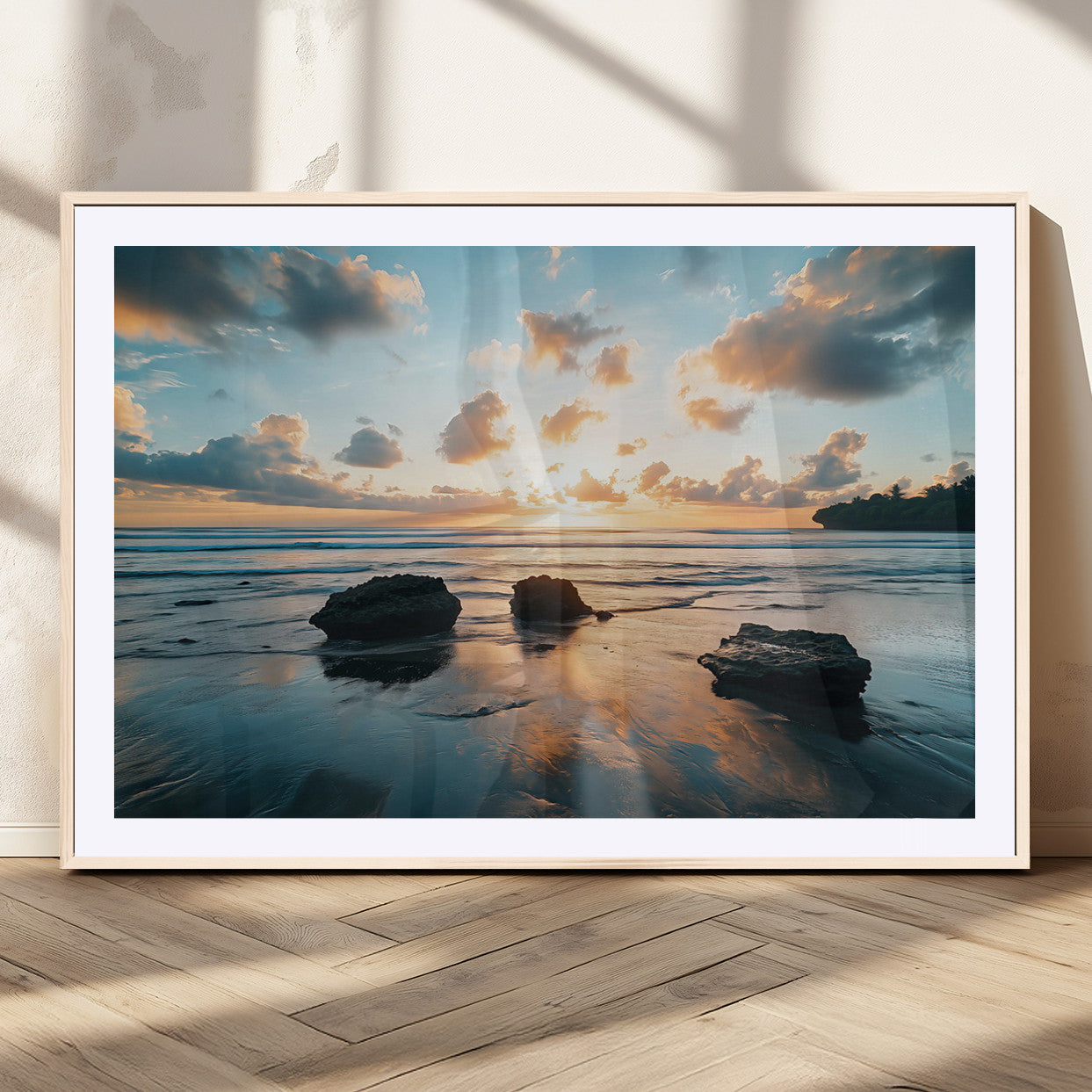 A serene beach at sunset with vibrant clouds, calm water, and rocks in the foreground reflecting the warm colors of the setting sun.