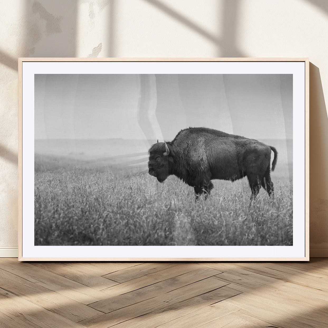 "Black and white image of a bison grazing in a vast field under an overcast sky."