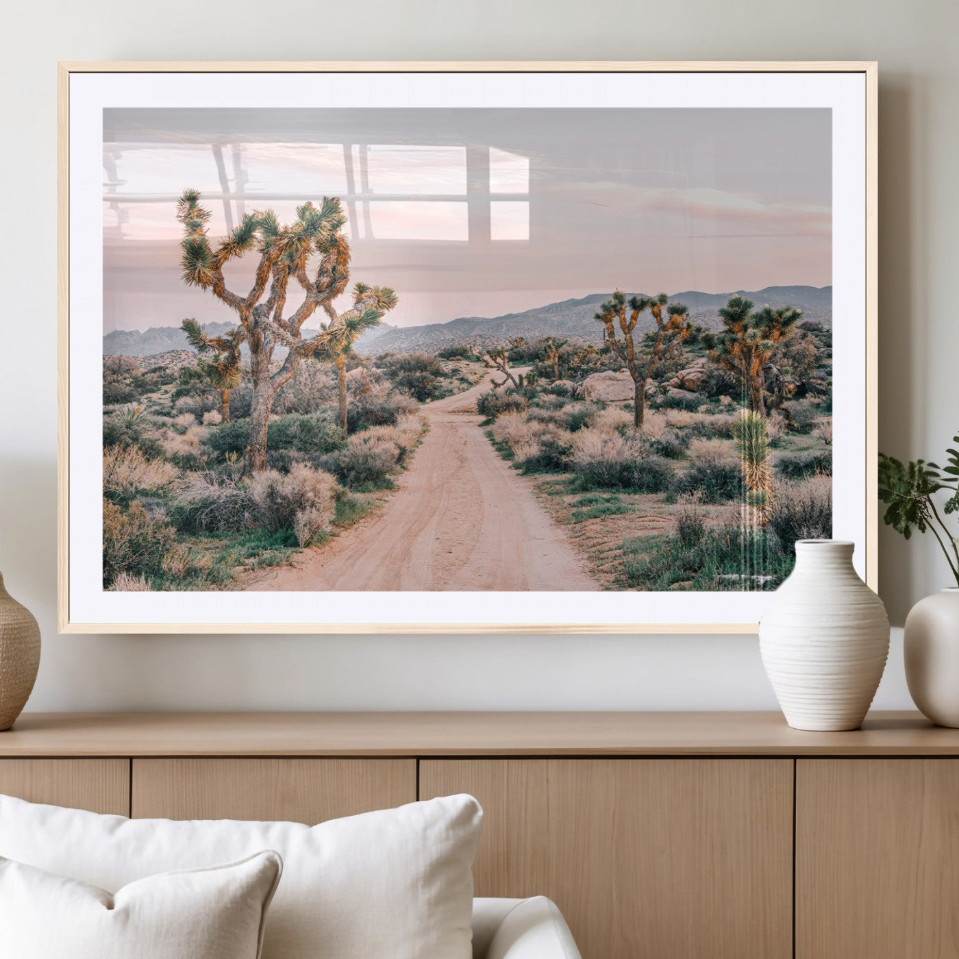 A dusty road winding through Joshua Tree National Park, framed by iconic twisted trees and warm desert tones under a soft pastel sky.