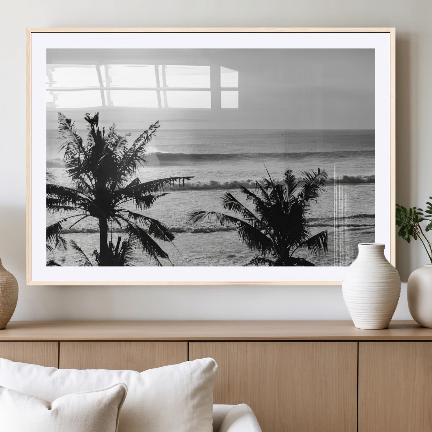 Black and white view of ocean waves crashing on a tropical coastline, framed by silhouetted palm trees under a vast, open sky.