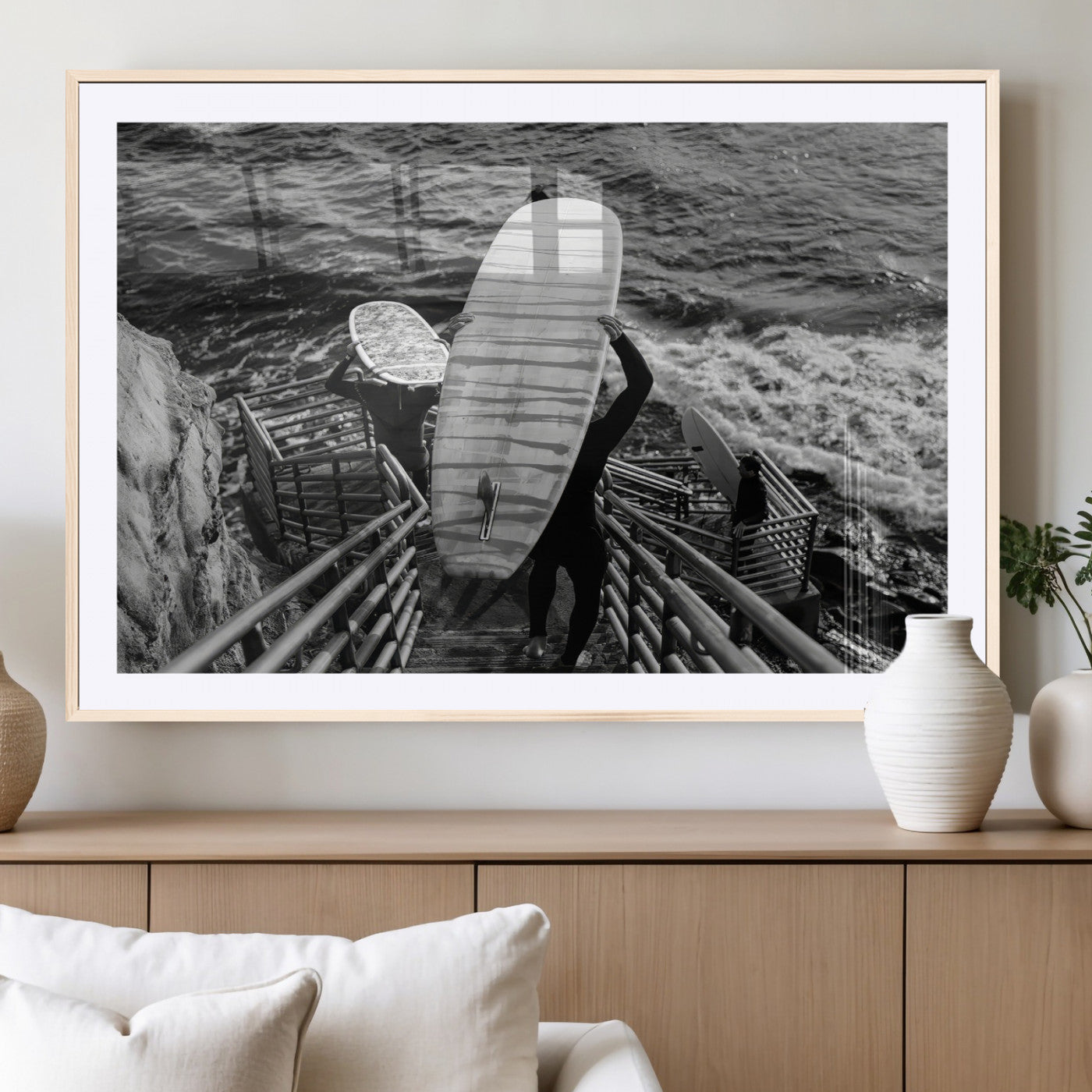 Black and white photo of surfers carrying boards down a rugged cliffside stairway, capturing a bold and adventurous coastal scene.