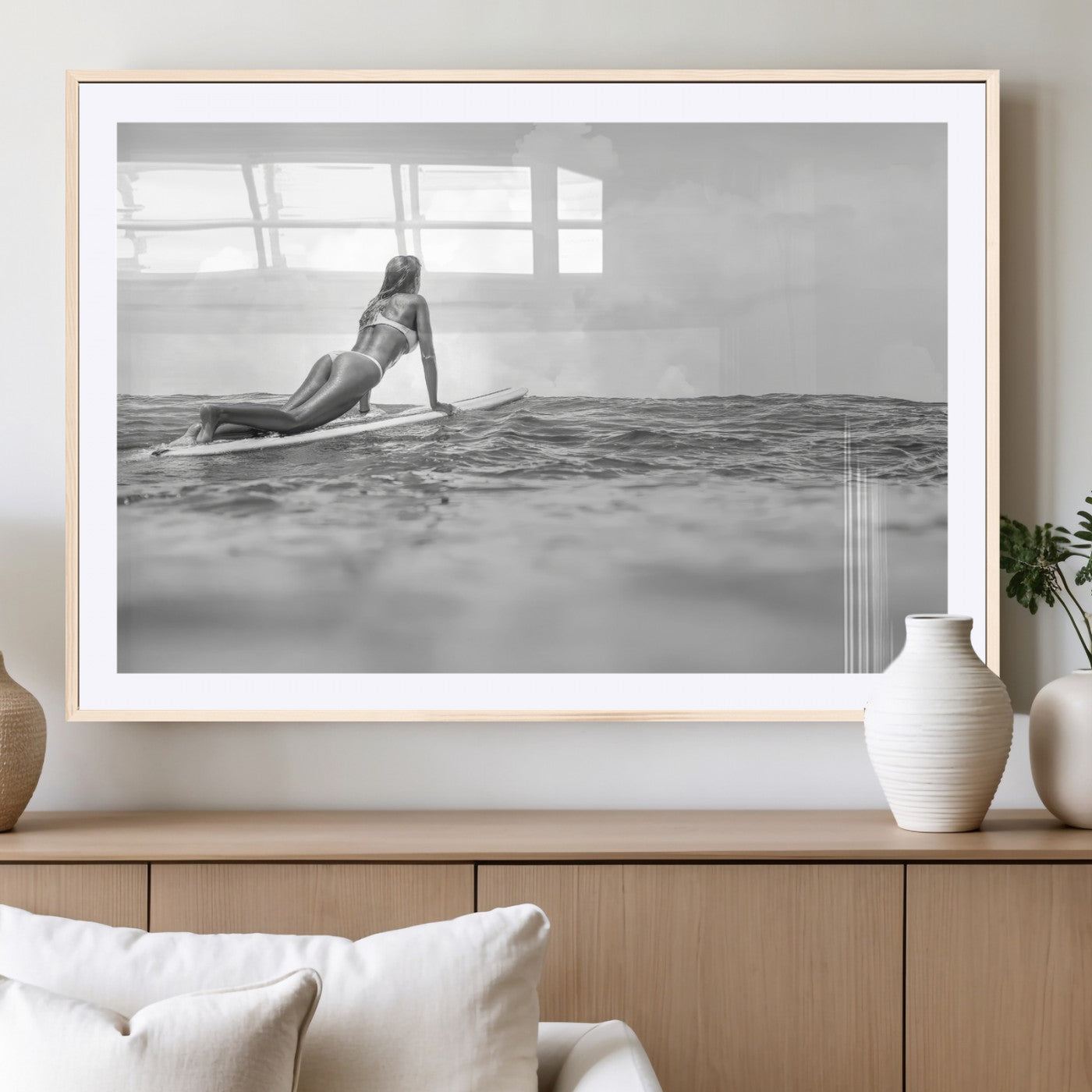 A black and white ocean scene featuring a surfer girl waiting on her board, gazing at the horizon, capturing a tranquil and adventurous coastal moment.