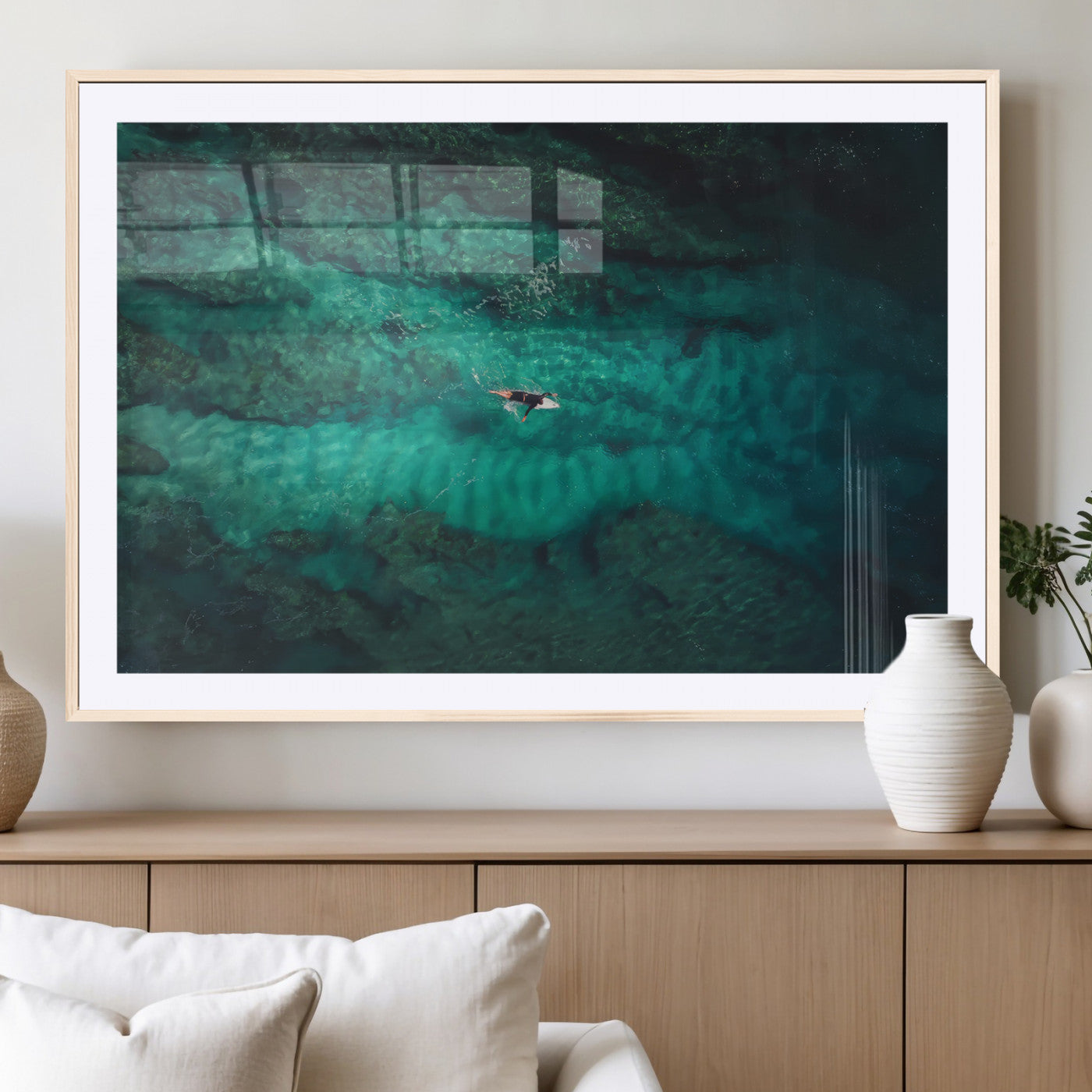 An aerial view of a solo surfer paddling through crystal-clear turquoise waters over a sunlit reef, capturing the beauty and serenity of open water surfing.